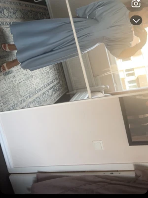 Ljusblå långklänning med vida ärmar - Säljer en elegant ljusblå långklänning med vida trekvartsärmar och rund halsringning. Klänningen har ett flowy fall och är tillverkad i ett mjukt, glansigt material som ger en lyxig känsla. Perfekt för dig som gillar stilrena och enkla plagg med mycket rörelse.