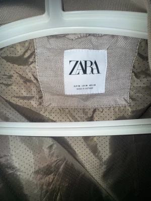 Beige bomberjacka från Zara - Snygg beige bomberjacka från Zara med ribbade muddar och krage. Jackan har dragkedja framtill och två sidofickor med dragkedja. Materialet är linneblandning med ett lätt glansigt foder. Perfekt för dig som gillar stilren och enkel design. Använd ett fåtal gånger.