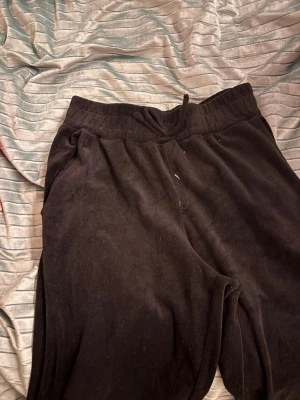 Svarta mjukisbyxor med snörning - Svarta mjukisbyxor med skön passform och snörning i midjan. Byxorna har muddar vid bensluten och är gjorda i ett mjukt material som känns riktigt chill. Perfekta för att hänga hemma eller dra till gymmet. Snygg enkel stil som funkar till det mesta.