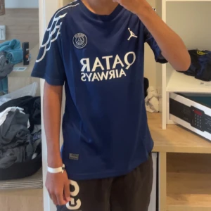 Blå PSG fotbollströja Jordan x Qatar - Snygg blå PSG fotbollströja från Jordan med Qatar Airways-tryck på bröstet och vita detaljer på axlarna. Klassisk rund hals och korta ärmar. Perfekt för dig som vill sticka ut på planen eller på läktaren.