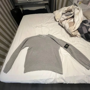 Grå stickad Stone Island tröja - Säljer en helt ny grå stickad tröja från Stone Island med klassisk rund hals och ribbade muddar. Tröjan har lång ärm och den ikoniska Stone Island patchen på vänster ärm. Perfekt för dig som gillar clean och stilren streetwear. Storlek M men passar L bra eftersom den är stor 