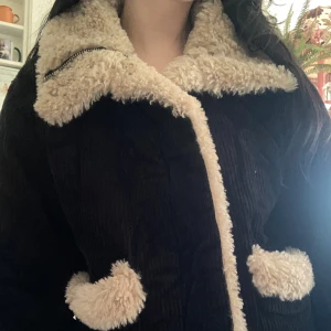 Svart teddyjacka från Topshop - Mysig svart teddyjacka från Topshop med fluffigt beige foder och stora slag. Jackan har dragkedja och två fickor med teddy-detaljer. Perfekt för kyliga dagar och ger en cool vintagekänsla.