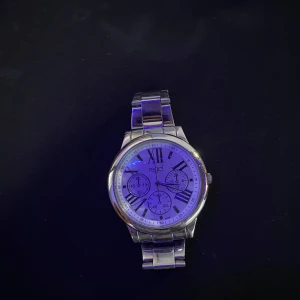 Silverfärgad klocka från Regal - Stilren klocka från Regal med rund urtavla i vitt och silverfärgat armband i metall. Urtavlan har romerska siffror och tre mindre visartavlor för extra funktioner. Perfekt accessoar för dig som gillar klassisk design med modern touch.