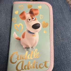 Secret Life of Pets  - Söt pennskrin med motiv från Secret Life of Pets och texten 'Cuddle Addict' i guld. Mintgrön bas med rosa kant och guldiga hjärtan. Inuti finns plats för pennor och tillbehör, allt matchar med gulliga djurmotiv och pastellfärger. Oanvänd 