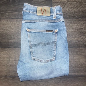 Nudie Jeans Lean Dean  - Säljer ett par Nudie Jeans Lean Dean i ljusblå tvätt med skinny passform. Jeansen har klassiska fem fickor, orangea sömmar och en liten slitning på vänster ben. Midja 40cm längd 101cm. Hål på högerknä som jag ej vet om det är defekt heller styling de får man avgöra med ögat själv :) JAG SKICKAR EJ FLER BILDER NÄR JAG BÄR JEANSEN! för storleksguide hänvisar jag till måtten och för bättre inblick i passformen rekommenderar jag att googla på modellnamnet :) S3