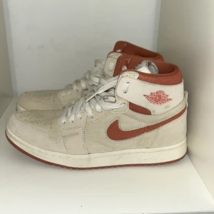 Pris kan diskuteras! Nike Air Jordan 1 Zoom Air beige/röd - PRIS KAN DISKUTERAS! Säljer ett par Nike Air Jordan 1 Zoom Air i beige mocka med röda detaljer och sula. Skorna har klassisk hög siluett, perforerad tåbox och snörning. Swoosh och insida i röd textil, samt Air Jordan-logga på sidan. Perfekta för dig som gillar streetwear och sneakers med retrovibe.