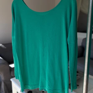 Grön långärmad blus   - Snygg grön långärmad tröja från Bik Bok i storlek XS. Tröjan har en rundad halsringning och en guldig dragkedja längs ryggen som cool detalj. Tillverkad i mjuk bomull, perfekt för lager-på-lager eller som den är.