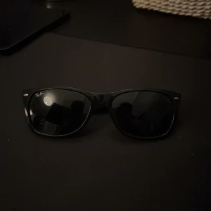Rayban solglasögon  - Bilderna visar ett par Ray-Ban Wayfarer solglasögon i svart. De har klassisk design och ser ut att vara i gott skick utan synliga repor eller skador. Perfekta för både vardag och soliga dagar. Snygg och tidlös modell från ett välkänt märke.