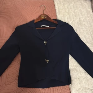 Mörkblå kavaj med dekorativa knappar - Snygg mörkblå mjuk kavaj från Zara med lång ärm och unik asymmetrisk skärning. Perfekt till jobb eller en utekväll. Har använts två gånger. 