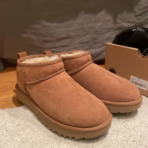 UGG Classic Ultra Mini Chestnut 36 - UGG Classic Ultra Mini i färgen chestnut, tillverkade i mjuk mocka med fluffigt foder av ull. Skorna har låg siluett, rund tå och grov yttersula i syntet. Perfekta för kalla dagar och ger en cozy vibe till din outfit. Hellllt oanvända.