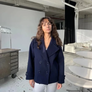 Marinblå kappa Design by Si - Säljer en marinblå kappa från Design by Si i storlek XS/S. Jackan har dubbelknäppning med stora knappar, bred krage och långa ärmar. Innefodret har lossat lite men inget som påverkar, går lätt att sy ihop. Ny pris 757kr