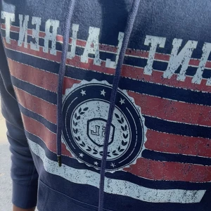 Saint Laurent hoodie - Säljer en marinblå hoodie från Saint Laurent med stort tryck framtill i rött, vitt och blått. Tröjan har snörning i huvan, känguruficka och långa ärmar. Size M men passar skulle säga den sitter som S. Den är nästintill ny då den är använd ett fåtal gånger men ingen prislapp eller förpackning tillkommer.