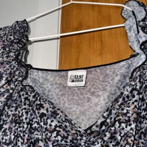 Mönstrad mesh topp från KA:NT - Säljer en topp  från KA:NT Copenhagen i storlek L. Toppen  har ett abstrakt mönster i svart, grått och lila toner, v-ringad hals och långa puffärmar med rynkade detaljer. Materialet är tunn och stretchig polyester som ger en snygg passform.