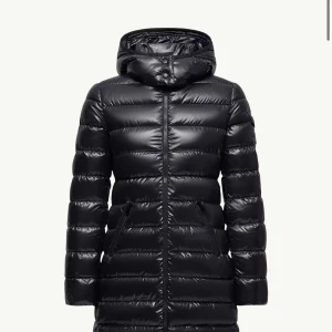 Svart lång jacka från Moncler - Säljer en svart, glansig lång jacka från Moncler med huva och dragkedja framtill. Perfekt för kalla vinterdagar och riktigt snygg passform. 