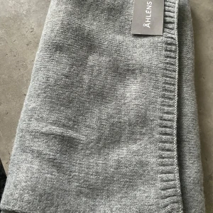 Grå stickad halsduk från Åhléns - Snygg grå stickad halsduk från Åhléns. Halsduken är mjuk och har en diskret ribbad kant längs ena sidan. Ny med prislapp 