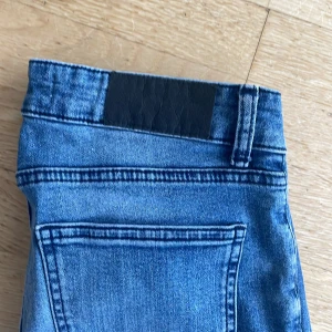 Blå skinny jeans med klassisk look - Snygga blå jeans med smal passform och klassisk femficksdesign. Jeansen har en mörkare tvätt med lätt slitning och raka bakfickor. Materialet är mjukt jeans och midjan är normal. Perfekt för dig som gillar en stilren och enkel look.