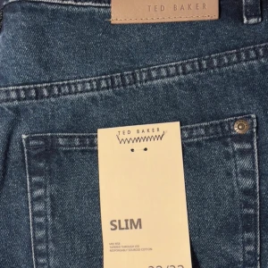 Slim jeans från Ted Baker, blå - Snygga slim jeans från Ted Baker i klassisk blå tvätt. Modellen har midwaist och smal passform med lätt avsmalnande ben. Jeansen är tillverkade av bomull och har klassiska fickor och detaljer i metall. Perfekta för dig som gillar stilrena och moderna jeans.