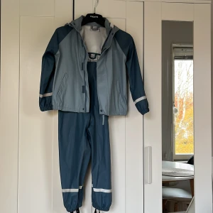 Blå täckbyxor med hängslen från EXA - Säljer blå täckbyxor från EXA Sweden med svarta justerbara hängslen och reflexdetaljer vid benslut. Byxorna är gjorda i slitstark syntet och har en hög midja för extra skydd mot väta. Perfekt för regniga och blåsiga dagar utomhus.Finns en litet defekt.