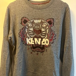 Grå Kenzo sweatshirt med tiger - Säljer en grå sweatshirt från Kenzo med ikoniskt broderat tigermotiv och logga på bröstet. Tröjan har rund halsringning och långa ärmar. Som ny 