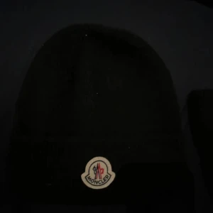 Svart Moncler mössa i ull - Svart mössa från Moncler med klassisk uppvikt kant och broderad logotyp framtill. Tillverkad i mjuk ull som håller dig varm under kyliga dagar. Enkel och stilren design som passar perfekt till vinterlooken.