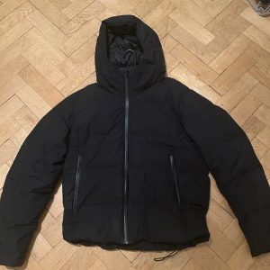 Svart pufferjacka från Uniqlo - Svart pufferjacka från Uniqlo med huva och hel dragkedja framtill. 10/10 skick använt 1 gång helt ny. Jackan har två snedställda fickor med dragkedja och en stilren, enkel design. Perfekt för kalla dagar med sin vadderade insida och klassiska look. Pris kan diskuteras 