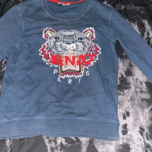 Blå Kenzo sweatshirt med tiger - Säljer en blå sweatshirt från Kenzo med det ikoniska tigerbroderiet och röd logga på bröstet. Tröjan har rund hals och långa ärmar, perfekt för dig som vill sticka ut med en cool streetstyle-look.