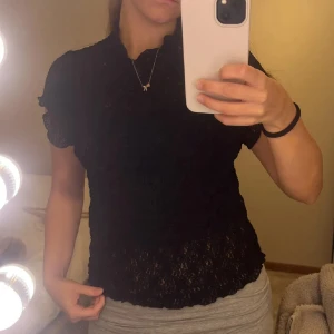 Svart spetsblus från Divided - Säljer en svart blus från Divided med spets och korta ärmar. Blusen har en söt liten volangkant vid halsen och är figurnära i modellen. En väldigt fin topp! Använd ungefär 3 gånger. Passar till fest men också annat.