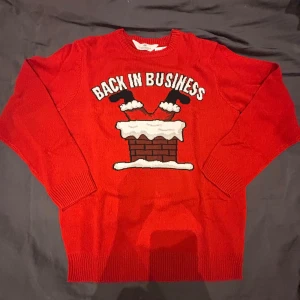 Röd jultröja H&M Back in Business - Rolig röd jultröja från H&M med texten 'Back in Business' och motiv av tomteben i skorsten. Tröjan är stickad, har rund hals och långa ärmar. Perfekt för att maxa julstämningen med en skön och färgstark look.