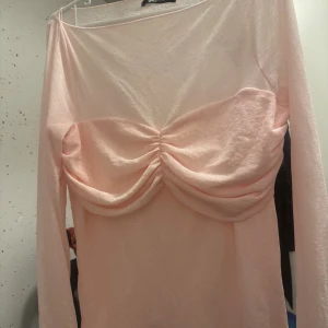 Ljusrosa långärmad topp med rynk - Säljer en ljusrosa långärmad topp från Gina Tricot med snygg rynkdetalj över bysten. Toppen har en tight passform och är tillverkad i mjuk bomullsmix. Perfekt för dig som gillar trendiga och feminina plagg.