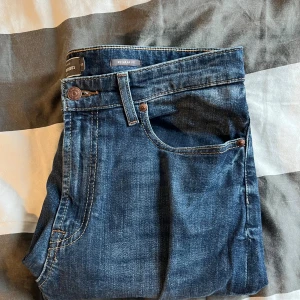 Blå regular fit jeans från Dressmann - Klassiska blå jeans från Dressmann i regular fit med fem fickor och snygga kontrastsömmar. Jeansen har en rak passform och är tillverkade i slitstarkt denimtyg som passar perfekt till en avslappnad stil.