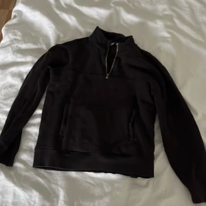 Svart half zip sweatshirt i bomull - Svart sweatshirt med half zip och hög krage. Tröjan har en stor ficka framtill och är tillverkad i mjuk bomull. Perfekt för chill dagar och enkel att matcha med jeans eller mjukisbyxor.