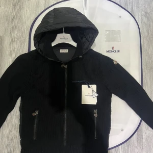 Moncler cardigan - Hej! Jag säljer nu en limited edition Moncler cardigan med en luva. Den är i jättebra skick endast andvänd 2/3 gånger och den har inte några defekter eller liknande. Den är äkta och köpt ifrån NK stockholm för inte så sedan och kvittot finns. Allt i bilderna ingår med jackan som moncler dustbag lapprna osv. Hör av er vid minsta lilla fråga! 👍