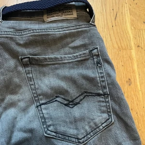 Replay grå jeans straight fit - Säljer ett par gråa Replay jeans med klassisk femficksdesign och raka ben. Jeansen har svarta sömmar på bakfickorna och en snygg Replay-logga. Materialet är mjukt jeans och midjan är normal. Perfekt för dig som gillar stilrena och bekväma jeans.