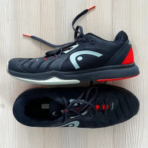 Svarta HEAD tennis sneakers stl 42 - Snygga svarta sneakers från HEAD med coola detaljer i rött och grått. Skorna har snörning, rund tå och en slitstark sula med mönster för extra grepp. Perfekta för träning eller sport, tillverkade i syntetmaterial med mesh för bra ventilation. Djur- och rökfritt hem. Stl 42