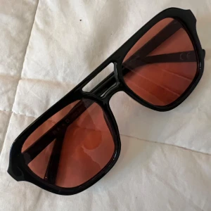  solglasögon  - Snygga svarta solglasögon från NA-KD med bred båge och coola orangefärgade glas. Modellen har en modern, kantig form och passar perfekt för dig som vill sticka ut. Ramen är i syntetmaterial och glasen har en mörk orange ton.