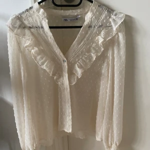 Vit volangblus från Zara  - Säljer en jätte söt blus från Zara som är lite genomskinlig i materialet med volanger vid v-ringningen och små söta prickar på blusen