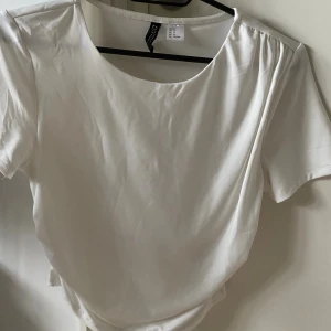 Vit t-shirt från Divided, storlek M - Säljer en snygg förgyrsydd  tshirt som formar kroppen snyggt, säljer den då den inte kommit till användning så mycket