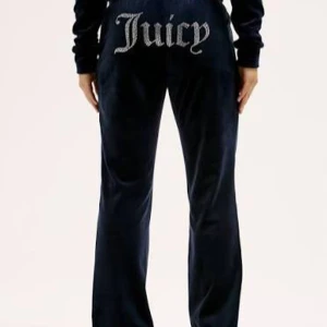Svarta velourbyxor Juicy Couture - Svarta mjukisbyxor i velour från Juicy Couture med glittrig Juicy-text baktill. Byxorna har en rak passform och är perfekta för en chill och trendig look. Supermjuka och sköna med klassisk Juicy-stil.