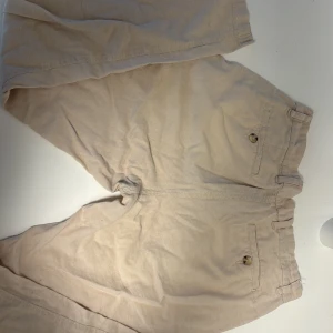 Beige linnebyxor från Jack & Jones. Pris kan diskuteras. - Snygga beige linnebyxor från Jack & Jones med klassisk passform och bälteshällor. De har två bakfickor med knappar och dragkedja fram. Tillverkade i ett mjukt bomullstyg som passar perfekt till varmare dagar. Skriv om ni har frågor.