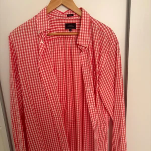 Rutig röd skjorta från boomerang - Säljer en klassisk röd och vit rutig skjorta från boomerang. Skjortan har lång ärm, knappar framtill och en snygg krage. Perfekt för dig som gillar tidlös stil med lite färg. Materialet är mjuk bomull som känns skönt mot huden.