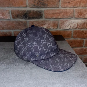 Gucci blå keps med GG-mönster - Snygg blå keps från Gucci med klassiskt GG-mönster över hela ytan. Justerbar rem baktill i blått skinn och insida i vit bomull. Perfekt för dig som vill ha en lyxig och trendig accessoar med tydlig logga och streetkänsla.