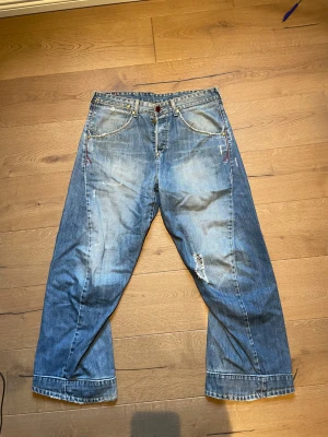 Levi's 501 blå wide jeans - Säljer ett par klassiska Levi's 501 jeans i blå tvätt med breda ben och slitningar på framsidan. Jeansen har hög midja, fem fickor och synliga sömmar. Materialet är robust denim och passformen är loose med en cool vintagekänsla.