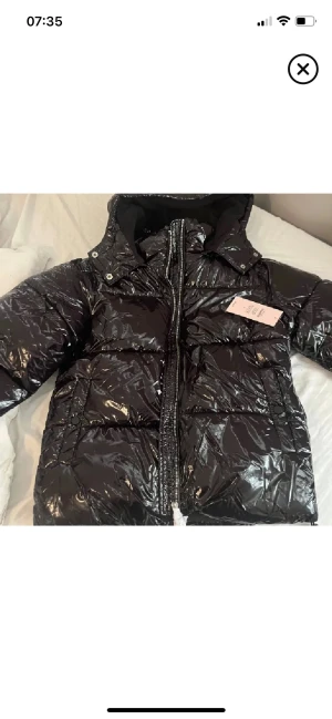 Glansig svart pufferjacka från Nelly - Säljer en svart, glansig pufferjacka med huva och dragkedja framtill från Nelly. Jackan är knappt använd och ser helt ny ut. Prislappen sitter inte kvar som på bilden men hör av er om ni har några fler frågor eller om ni vill ha fler bilder. Jackan är i XS men skulle säga att den passar S oxå💕