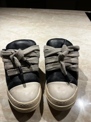 Rick Owens svarta sneakers med bred snörning - Säljer ett par svarta och vita Rick Owens sneakers med breda grå snören .  Jag säljer för de passar inte mig längre och dem är äkta ny pris är 9000 kr men har tyvärr inte box eller kvitto för fick det av en vän men om det finns något sätt att visa att de är äkta så skriv gärna. Men mitt pris är 2000 för ja har tyvärr inte något som visar att de är äkta så skriv till mig om ni är intresseradade 😁Perfekt för dig som gillar statement sneakers med unik design.