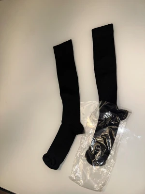 Svarta knästrumpor S/M stödstrumpor  - Svarta, långa knästrumpor i enkel och stilren design. Perfekta att bära till kjol eller shorts för en clean look. Strumporna är stretchiga och sitter skönt på benet.När vi sitter eller står länge kan ben och fötter svullna upp och kännas tunga. Även graviditet, övervikt och flygresor kan orsaka svullna fötter och ben. Svullnaden kan ofta motverkas med motion och kompression med stödstrumpor. Kompressionsstrumpor är också bra att använda vid längre flygresor, eftersom långvarigt sittande i luften