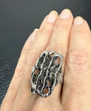 Stor silverfärgad statementring - Vintage ring i silvrig metall med grov, skulptural form i brutalistisk stil. Troligen ett studiosmycke från 60-/70-talet, eventuellt ännu äldre. Gedigen känsla med fin patinering. Mått: ca 3,3 cm hög, 2 cm bred, innerdiameter ca 1,7 cm. Jag prutar inte – men erbjuder rabatt vid köp av flera saker. Rensar smyckeskrin & garderob – kika gärna på mina andra annonser! 