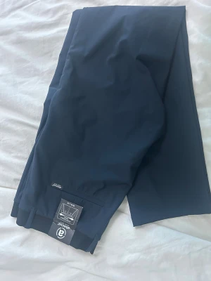 Mörkblå byxor från Abacus W34 L34 - Golfbyxor Snygga mörkblå byxor från Abacus med rak passform och stilren design. Materialet är mjukt och lätt, perfekt för dig som gillar sportiga och funktionella plagg. Diskret logga på insidan och klassisk midja. Passar dig som vill ha en clean look.