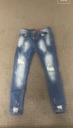 Blå Dsquared2 skinny jeans med slitningar - Snygga blå jeans från Dsquared2 med slitna detaljer och blekta partier på både fram- och baksida. Modellen är skinny med låg midja och klassiska fem fickor. Jeansen har orange Dsquared2-märke bak och röd logga vid gylfen. Perfekt för dig som gillar streetstyle.