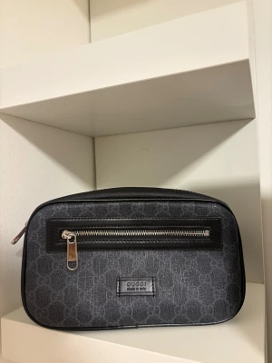 Gucci magväska / wastebag - Snygg svart axelväska från Gucci med klassiskt GG-mönster och silverfärgade dragkedjor. Väskan har en rektangulär form, justerbar axelrem i rött och blått, samt detaljer i skinn och textil. Perfekt för dig som vill ha en stilren och lyxig accessoar. Först till kvarn 1800kr