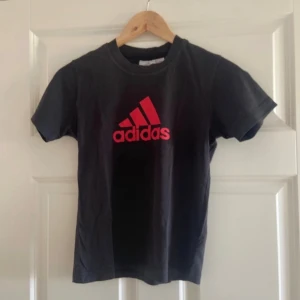 Svart Addidas t-shirt,tröja med rött tryck - Svart t-shirt från Adidas med klassiskt rött logotryck på bröstet. Rund hals och korta ärmar, tillverkad i mjuk bomull som är skön mot huden. Perfekt för dig som gillar sportig och enkel stil med tydlig branding.funkar till xs-m.har även andra hoddie och rosa och annat.